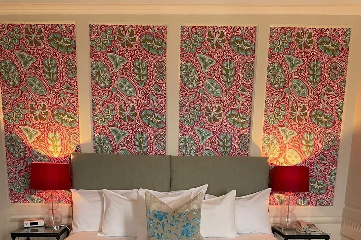 A neatly made bed with a striped bedspread and two pillows, a red lamp on each side, and a patterned wallpaper on the walls.
