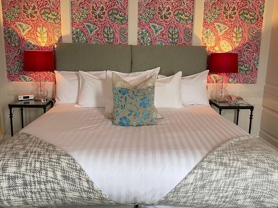 A neatly made bed with a striped bedspread and two pillows, a red lamp on each side, and a patterned wallpaper on the walls.