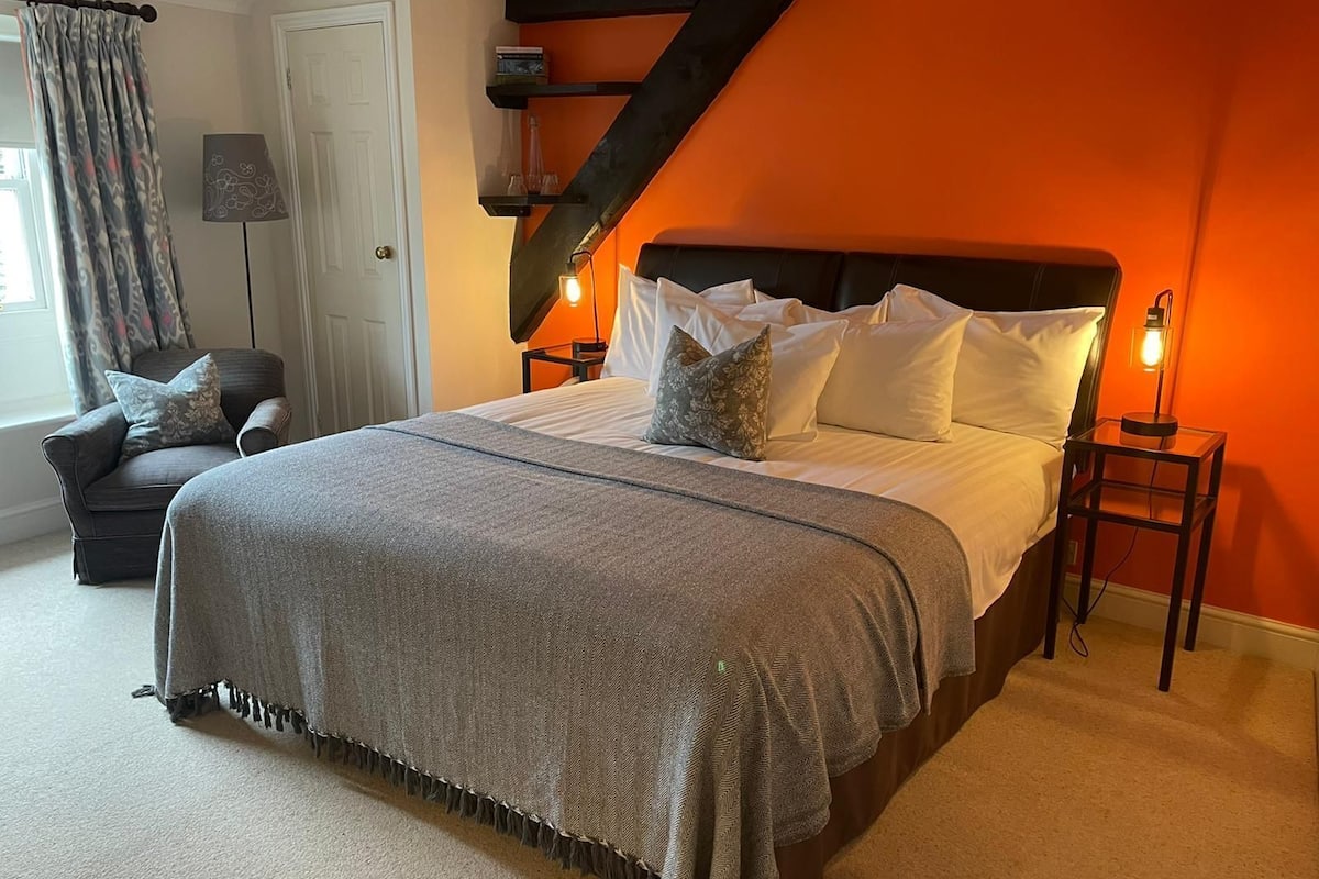 A bedroom with a bed, a chair, a lamp, and a shelf.