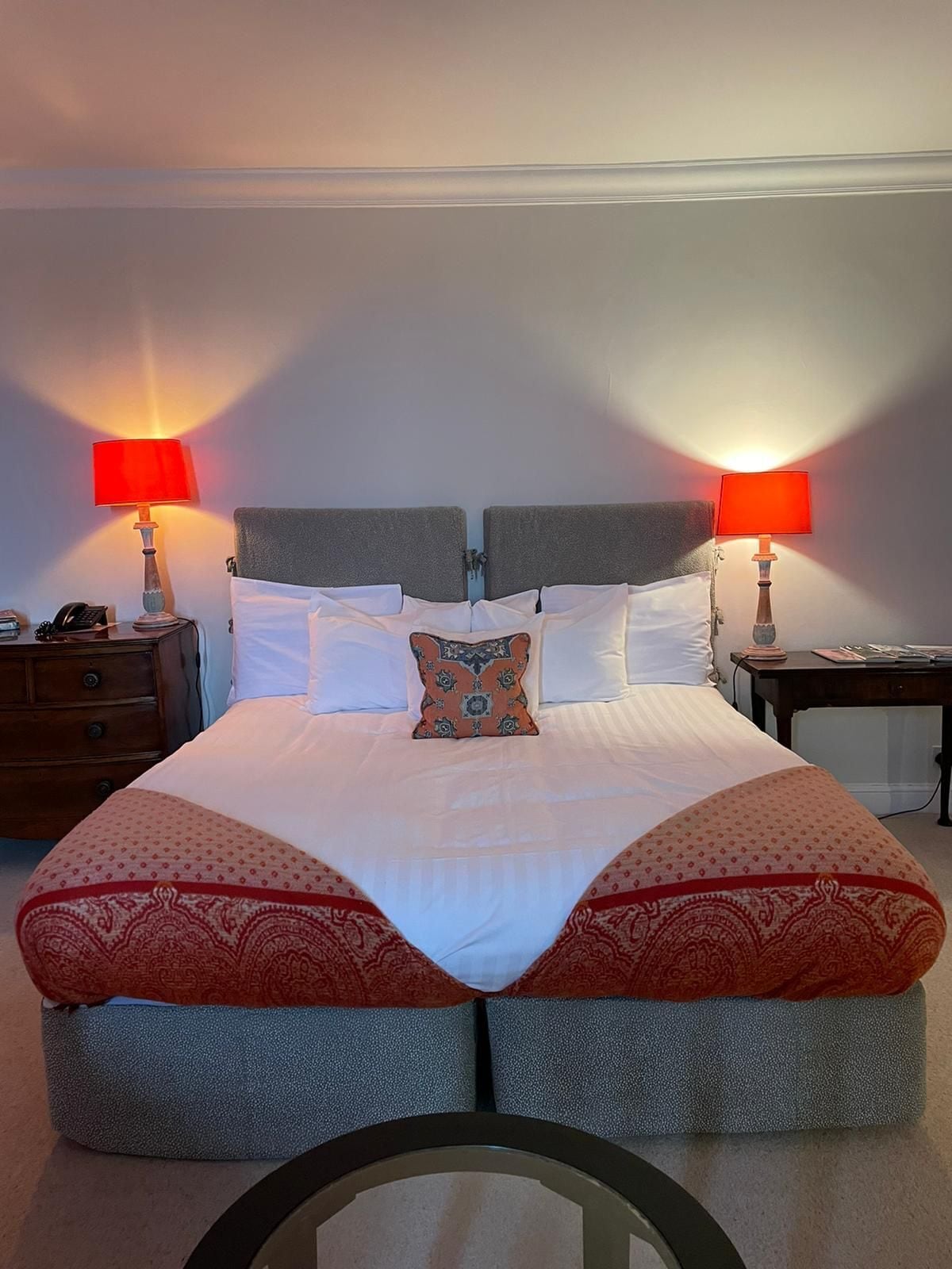 A neatly made bed with two pillows, a bedside table with a lamp, and a nightstand with a phone.