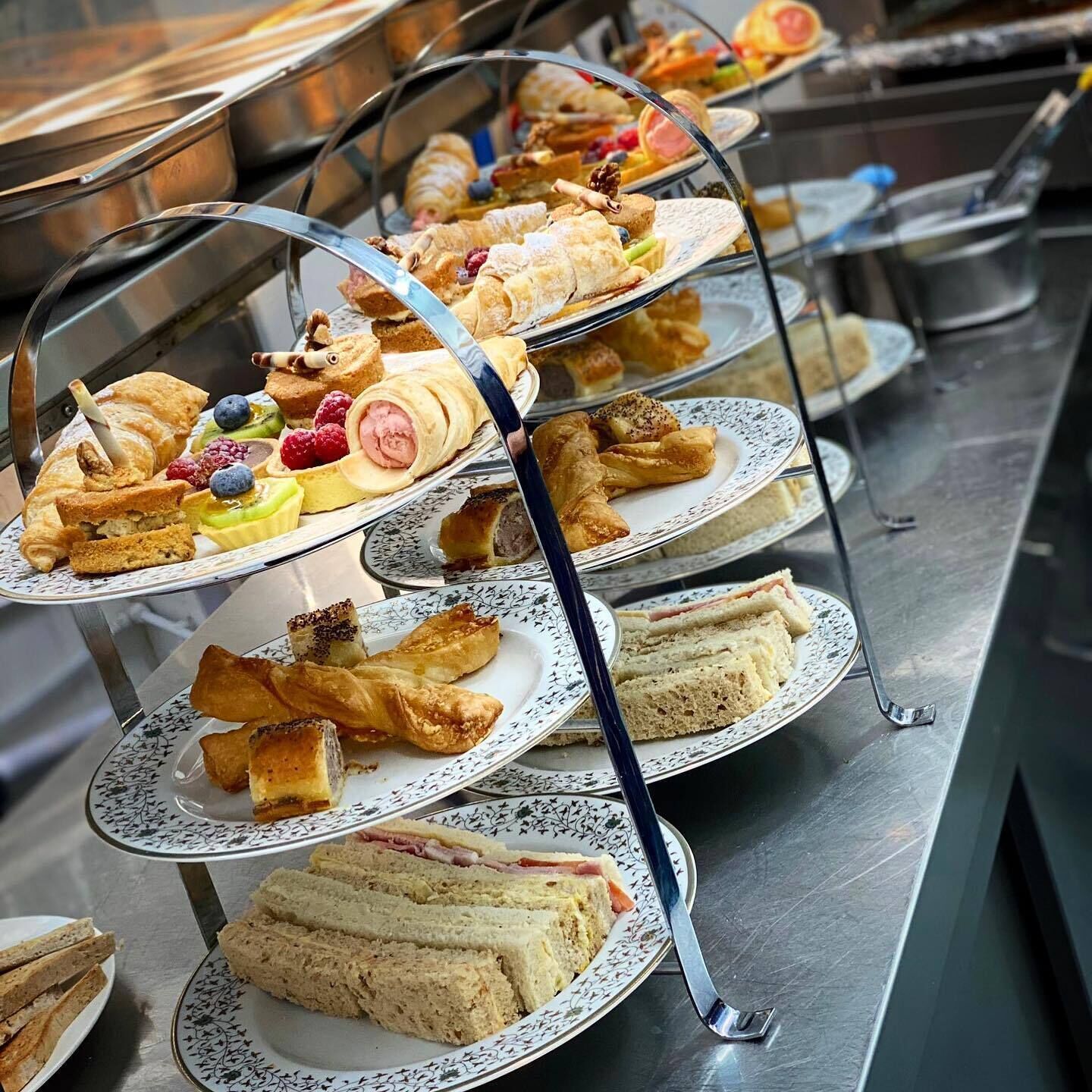 A buffet with multiple trays of food including pastries, sandwiches, and fruit.