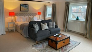 A cozy bedroom with a bed, a grey sofa, a wooden chest, and a window with curtains.