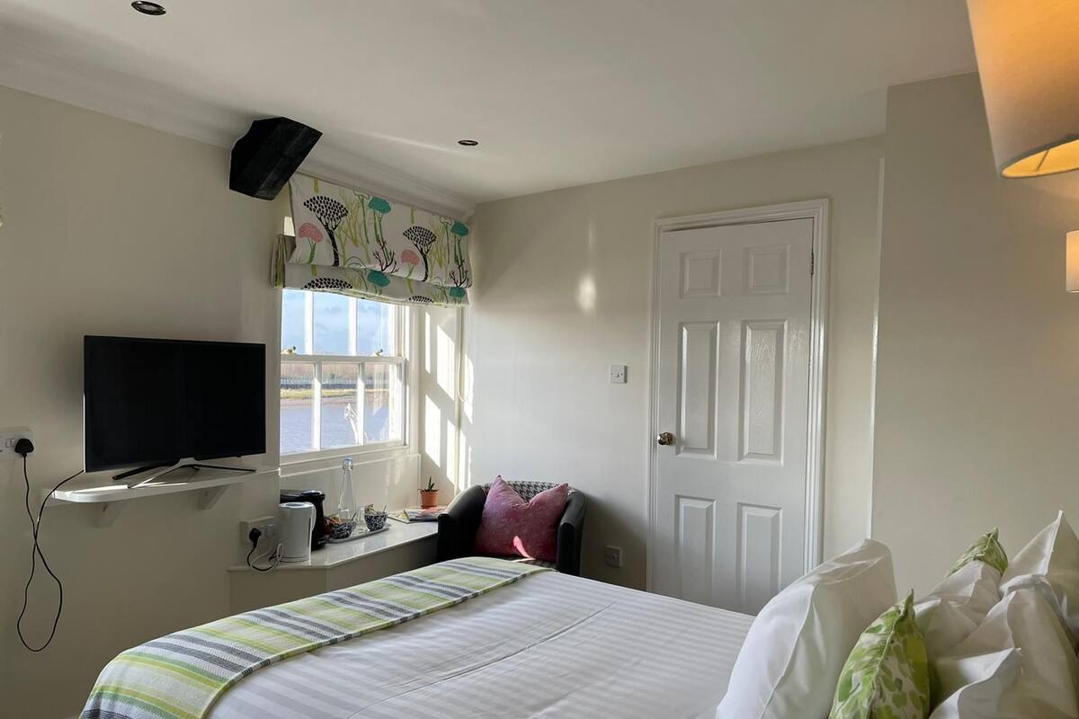 A bedroom with a bed, a TV, a window with curtains, a door, and a lamp.
