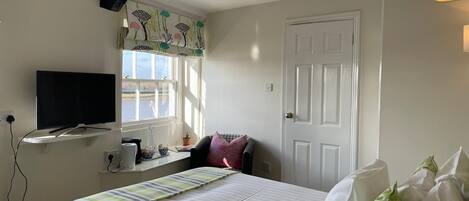 A bedroom with a bed, a TV, a window with curtains, a door, and a lamp.