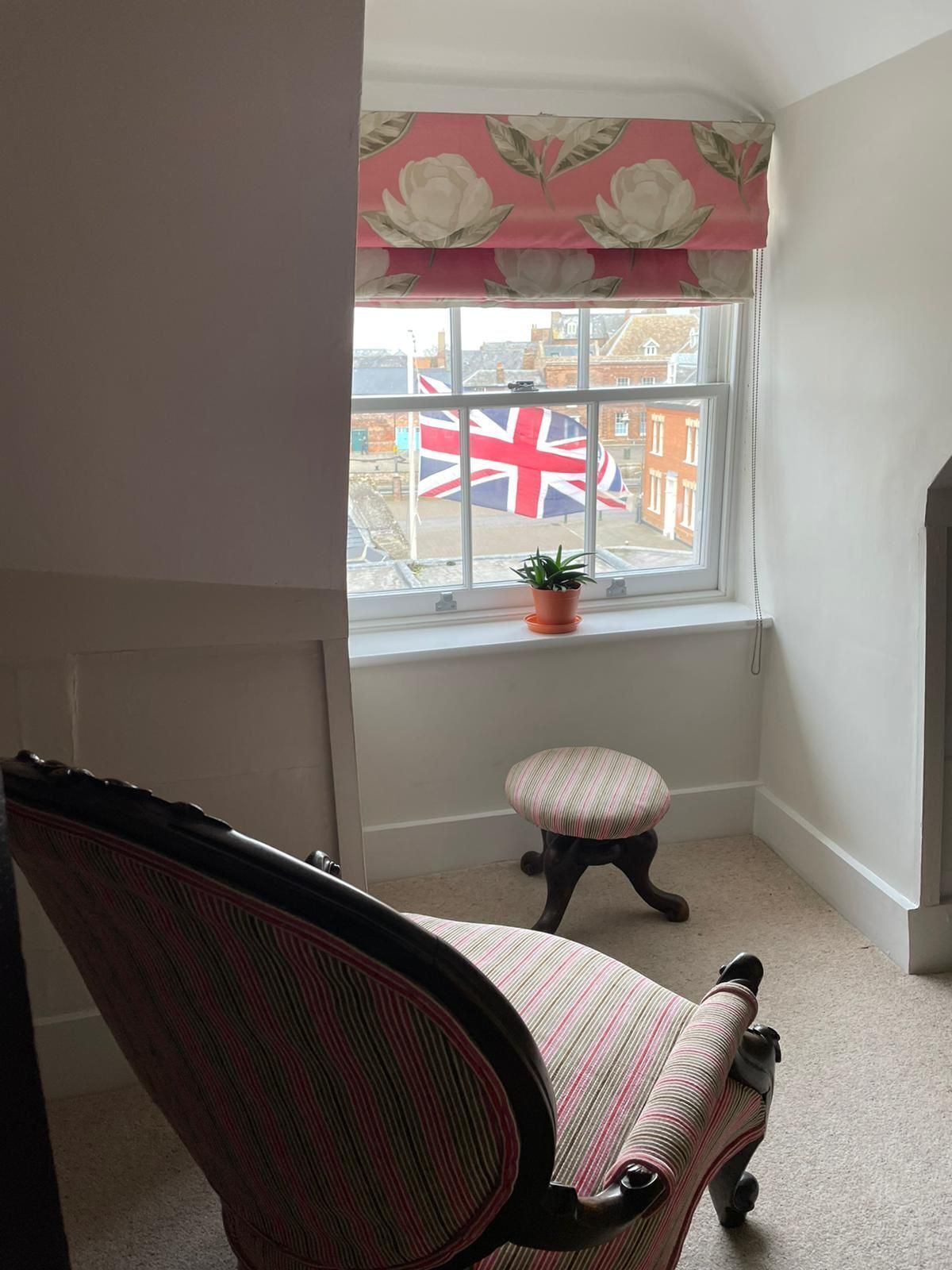 Une pièce d’angle avec une fenêtre, une chaise et une petite table sur laquelle est posée une plante en pot.
