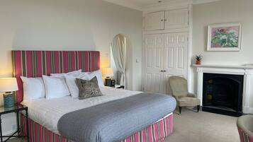 A bedroom with a large bed, a chair, a fireplace, and a door.