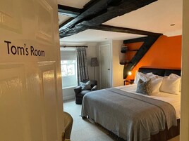 Un dormitorio con una cama, una silla, una mesita de noche y un ventanal con cortinas.