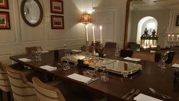 Un comedor elegante con una larga mesa dispuesta para varios invitados, que incluye un espejo, cuadros enmarcados y una araña.