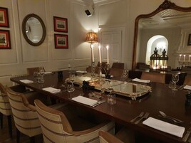 Un comedor elegante con una larga mesa dispuesta para varios invitados, que incluye un espejo, cuadros enmarcados y una araña.