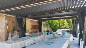 An outdoor covered dining area with white tables and chairs, a grill, and a view of greenery. - Large 600M2 property, tennis and 60sqm pool house with bar-kitchen on 10000 sqm (Mougins)