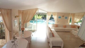 A spacious living area with a pool view, a sofa, and a dining table with wine glasses. - Large 600M2 property, tennis and 60sqm pool house with bar-kitchen on 10000 sqm (Mougins)