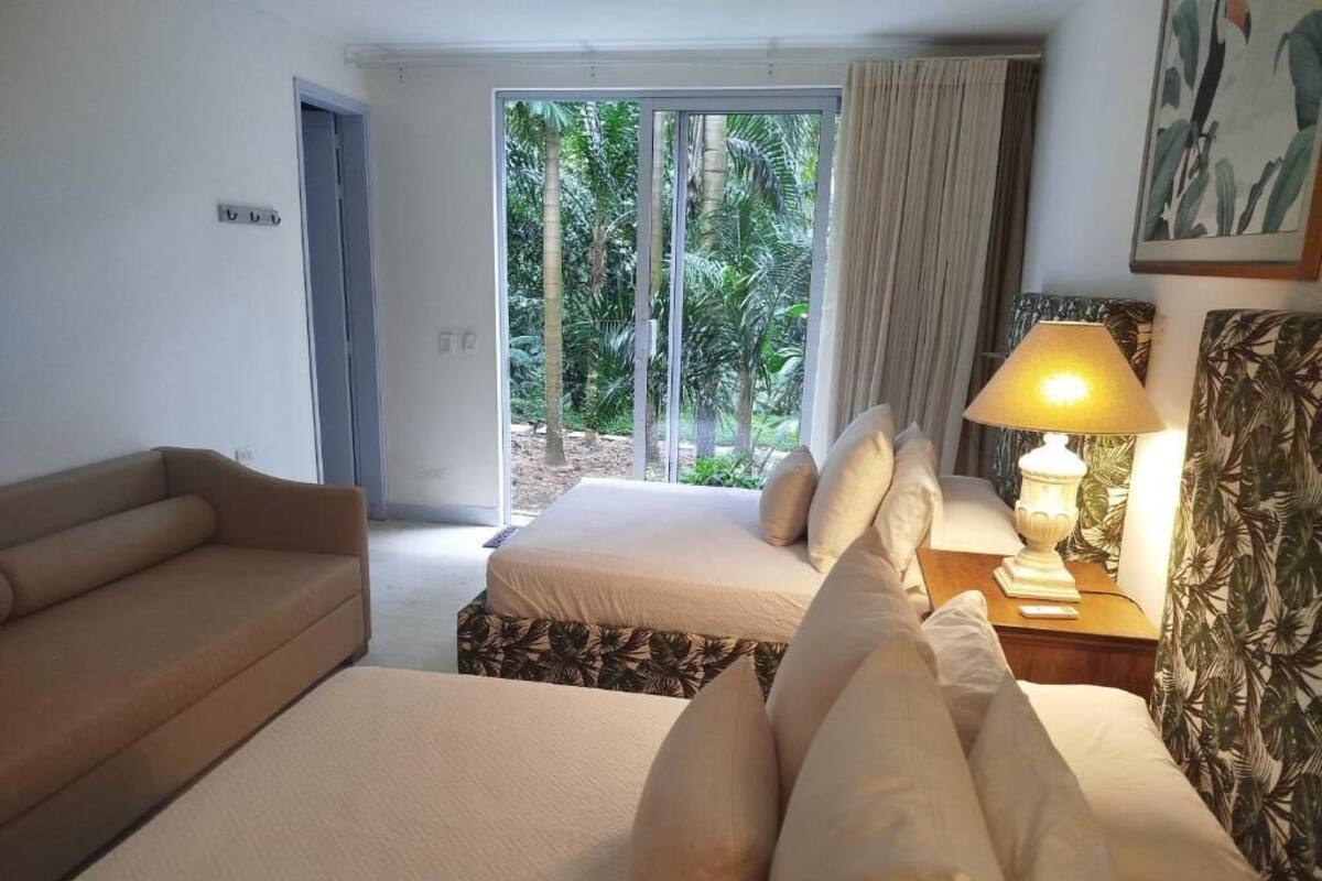 A hotel room with a bed, a sofa, a lamp, and a view of palm trees through a sliding door.