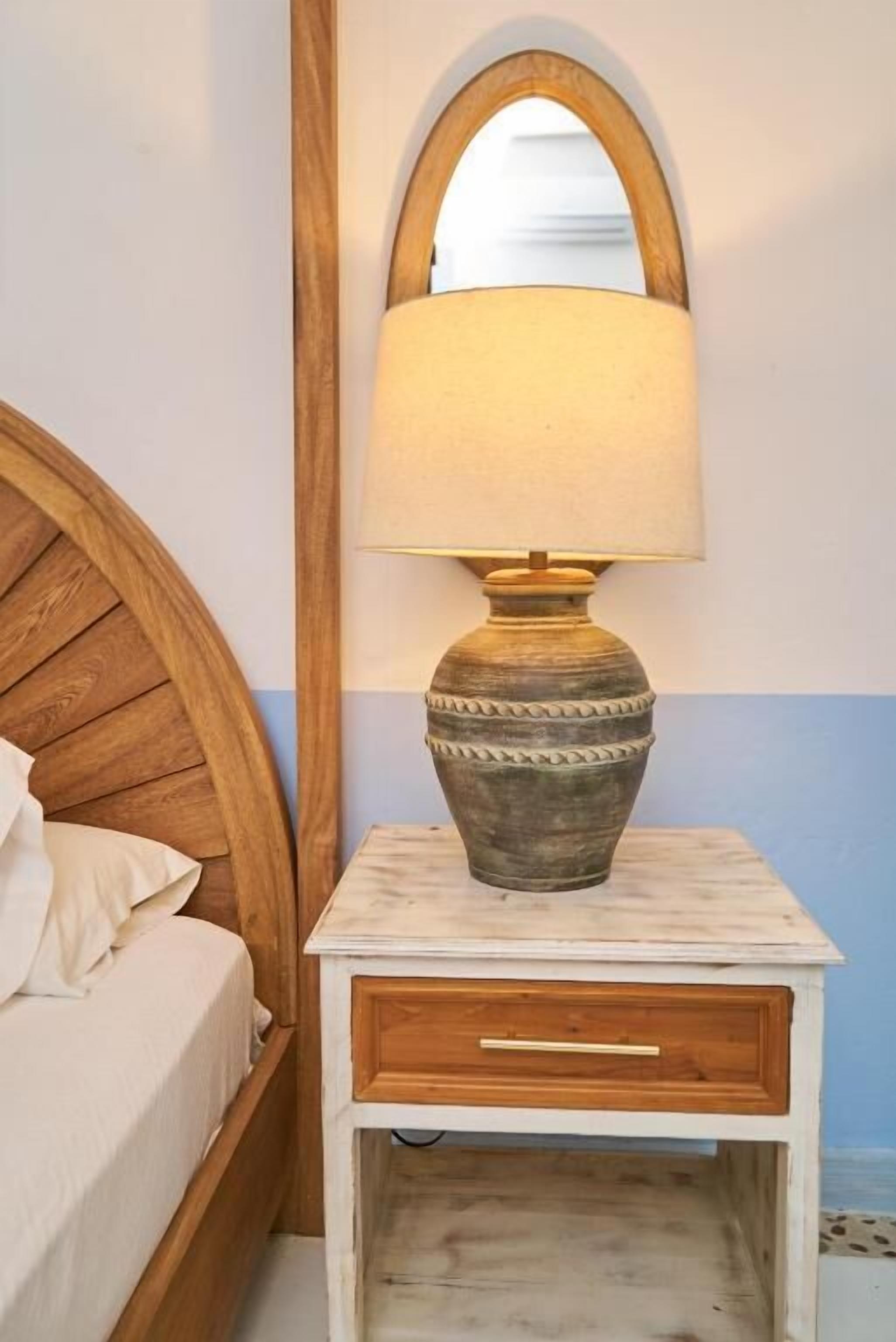 Una cama de madera con cabecera, una mesita de noche con lámpara y un espejo.