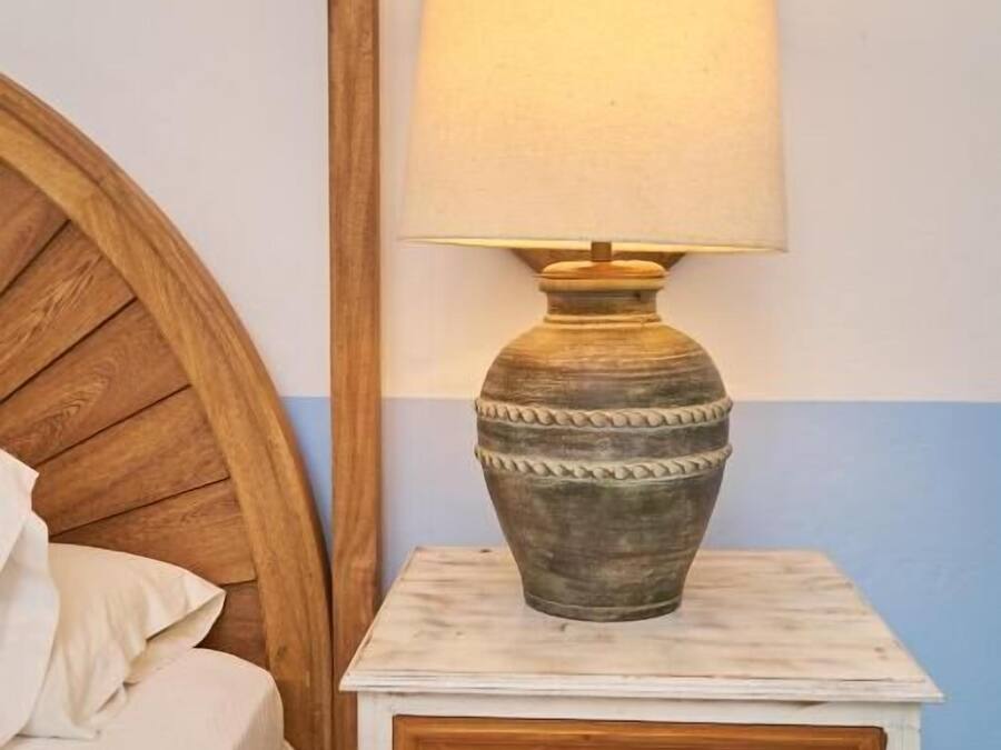 Una cama de madera con cabecera, una mesita de noche con lámpara y un espejo.
