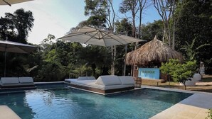 Una piscina con sillas de descanso y una estructura con techo de paja que dice 'EL BOSQUE'.