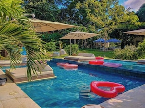Ein Pool mit Liegestühlen und Sonnenschirmen, umgeben von viel Grün.
