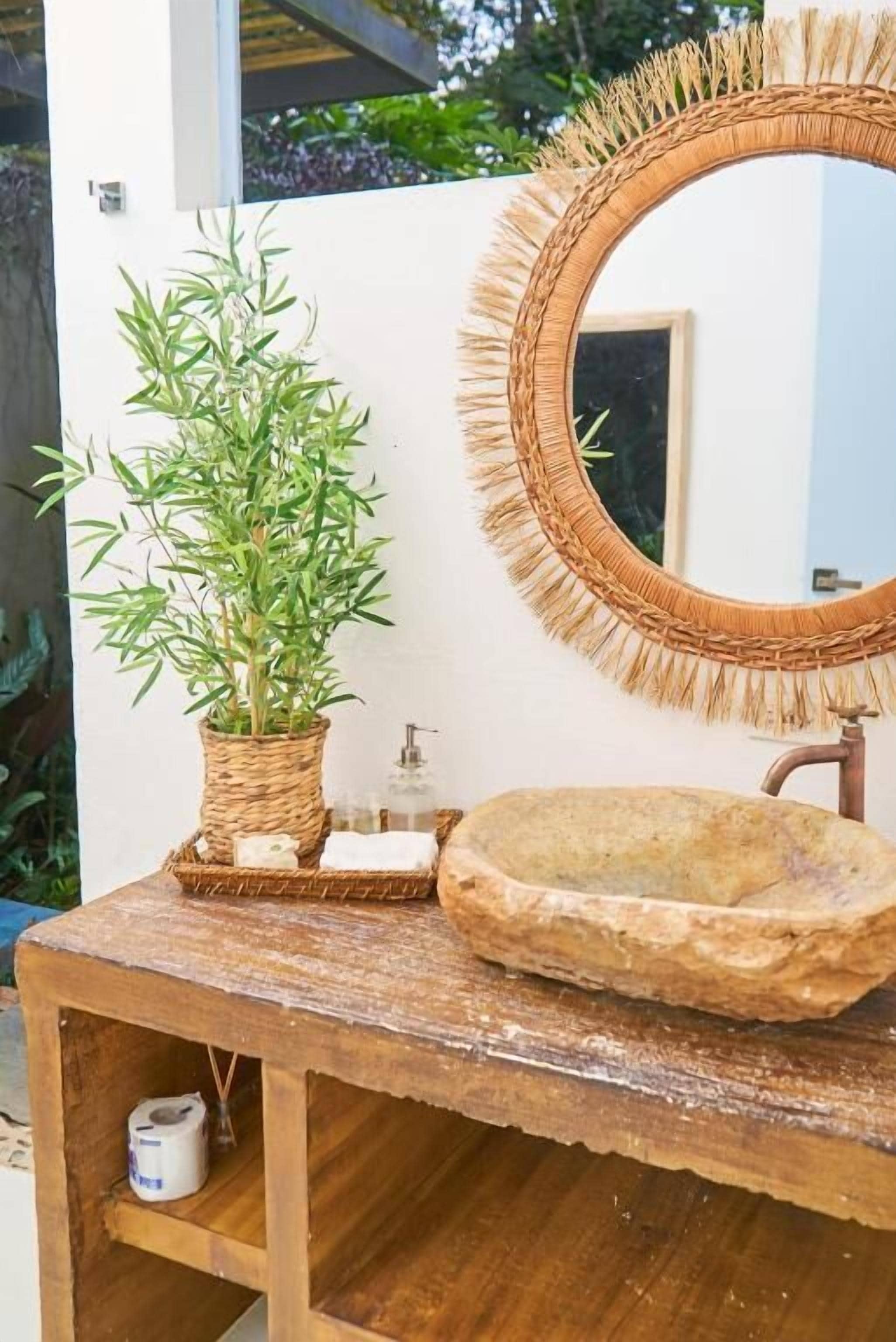 Une salle de bain rustique avec un miroir en osier, un lavabo en pierre et une plante en pot.