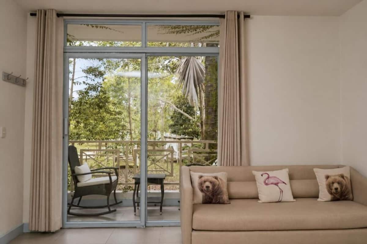 Una habitación con puerta de cristal corredera que da a un espacio exterior, un sofá con dos almohadones y una silla.
