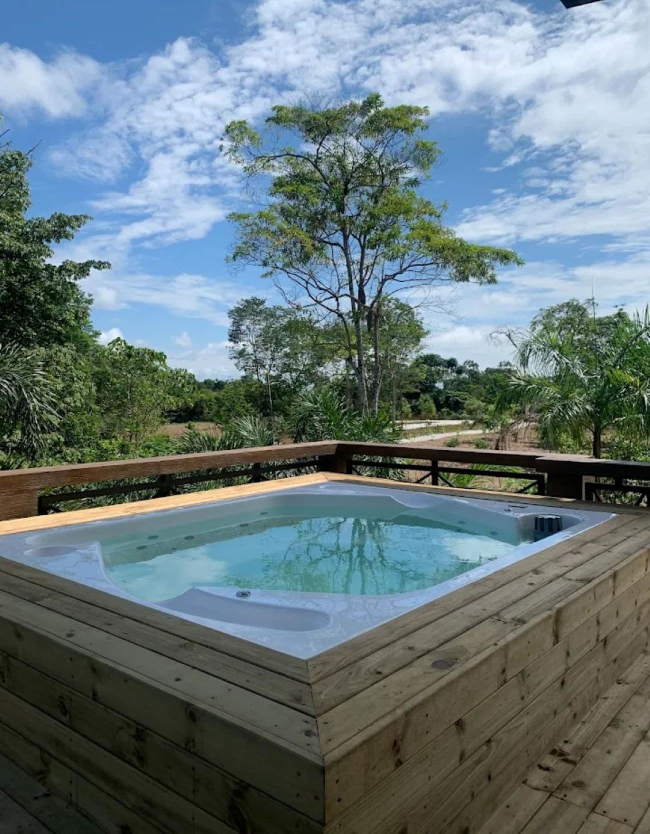 A hot tub on a wooden deck with a view of trees and a clear sky.