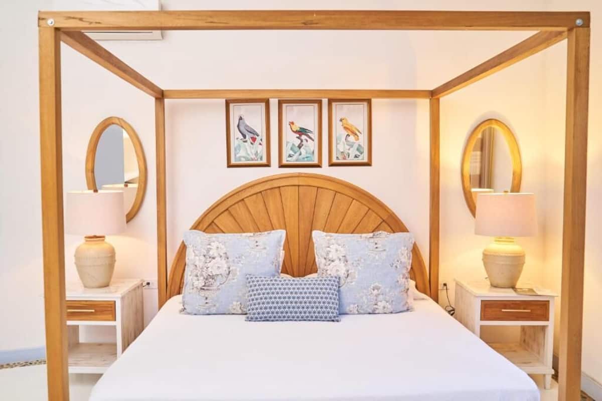Un dormitorio con cabecera de madera, dos mesitas de noche con lámparas y tres cuadros enmarcados con pájaros en la pared.