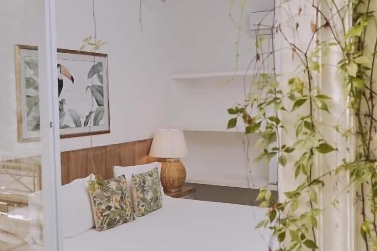 Un dormitorio con cama, mesita de noche, lámpara y estante en la pared.