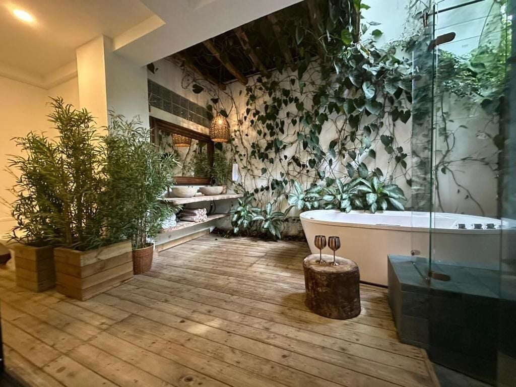 Suelo de madera, plantas en macetas, una bañera y una pared con plantas trepadoras.