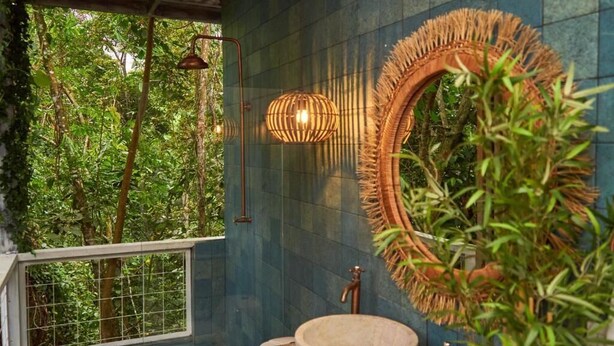 Un baño con un espejo grande, un lavabo de madera y vistas a vegetación exuberante.