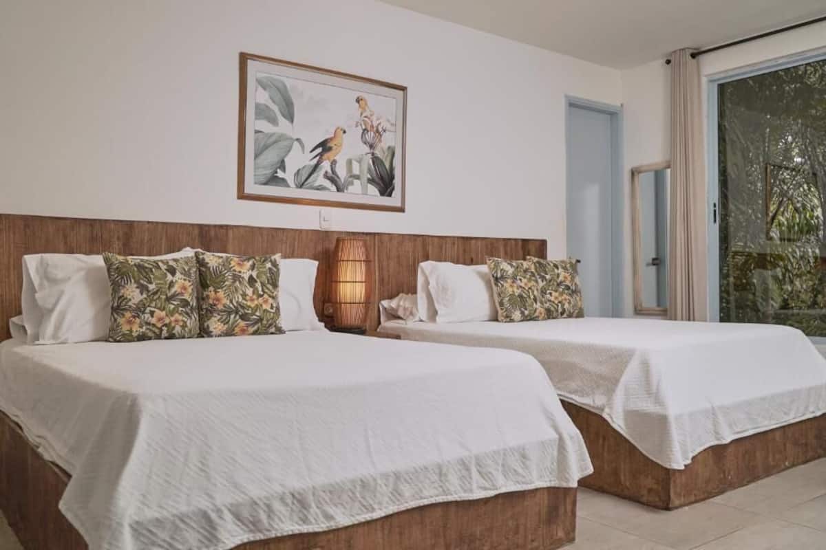 Habitación de hotel con dos camas, cabecero de madera, un cuadro enmarcado en la pared y una puerta corrediza de vidrio que da a un balcón.