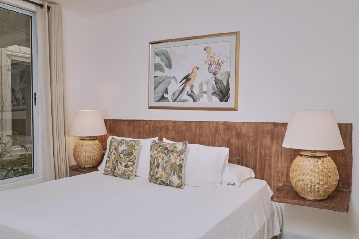 Une chambre d’hôtel avec un lit, deux lampes fixées au mur, un tableau représentant des oiseaux et une fenêtre avec des rideaux.