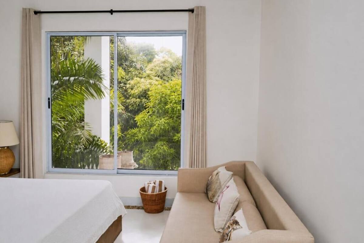 Una habitación con cama, sofá, ventana con cortinas y vistas al exterior.