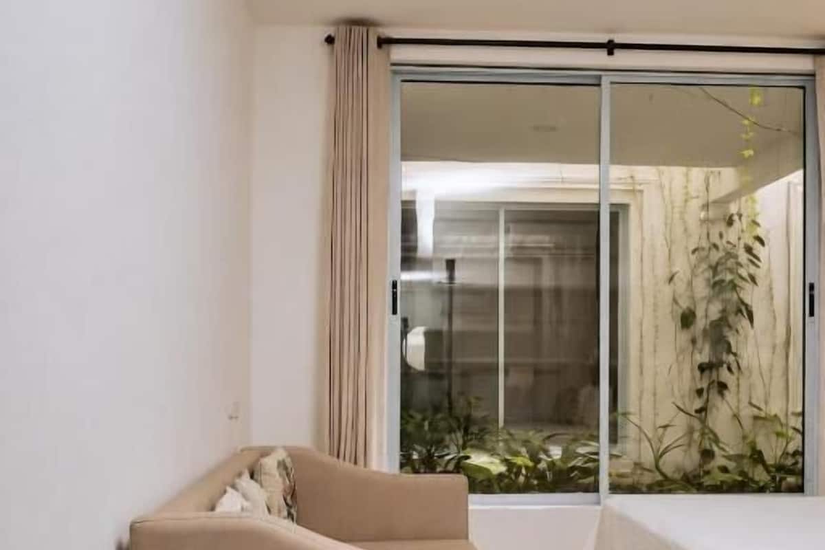 Un dormitorio con cama, sofá, puerta corrediza de vidrio y vista a la vegetación.