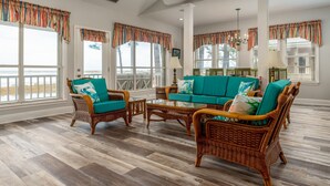 A spacious room with wicker furniture, large windows, and a view of the beach. - Screamin' Peace 1614 Cadillac 3 Bedroom Home by RedAwning (Dauphin Island)