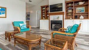 A spacious living room with wicker furniture, a fireplace, and a television mounted above it. - Screamin' Peace 1614 Cadillac 3 Bedroom Home by RedAwning (Dauphin Island)