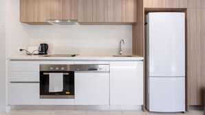 A modern kitchen with a built-in oven, dishwasher, and a white refrigerator. - Stirling Apartment 1- Modern Central Apartment (Yokine)