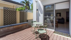 A patio with a table and chairs, a sliding glass door leading to a living area, and a decorative fence. - Stirling Apartment 1- Modern Central Apartment (Yokine)