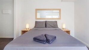 A neatly made bed with a folded towel, two bedside lamps, and a mirror above the bed. - Stirling Apartment 1- Modern Central Apartment (Yokine)
