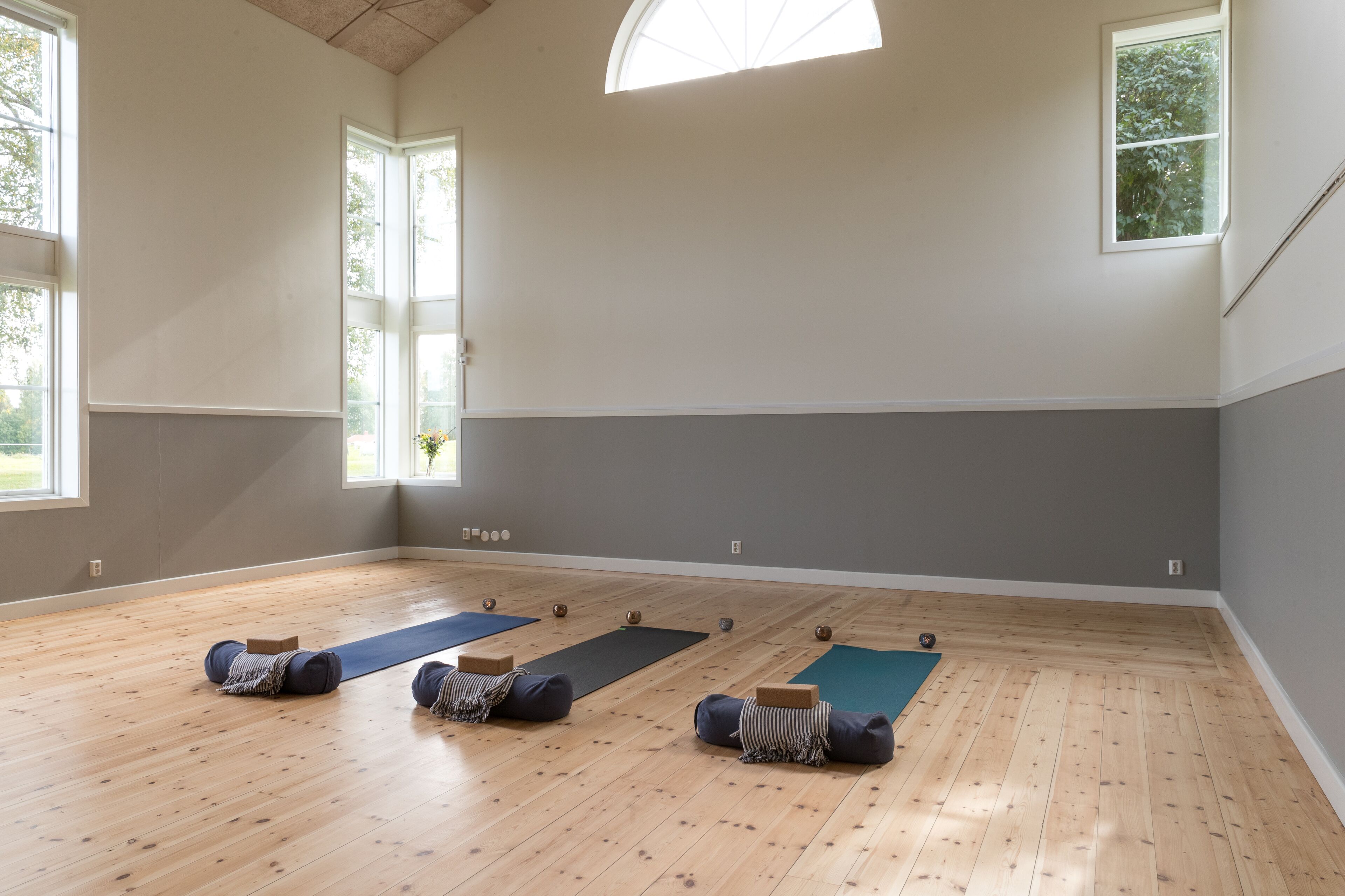 Ein geräumiges Zimmer mit Holzboden, großen Fenstern und Yogamatten.