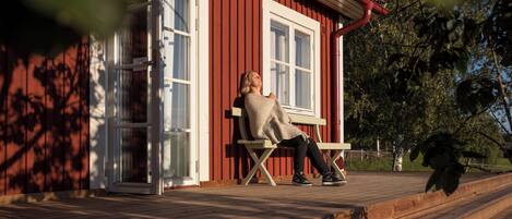 A person sitting on a bench outside a red building with white trim and large windows.