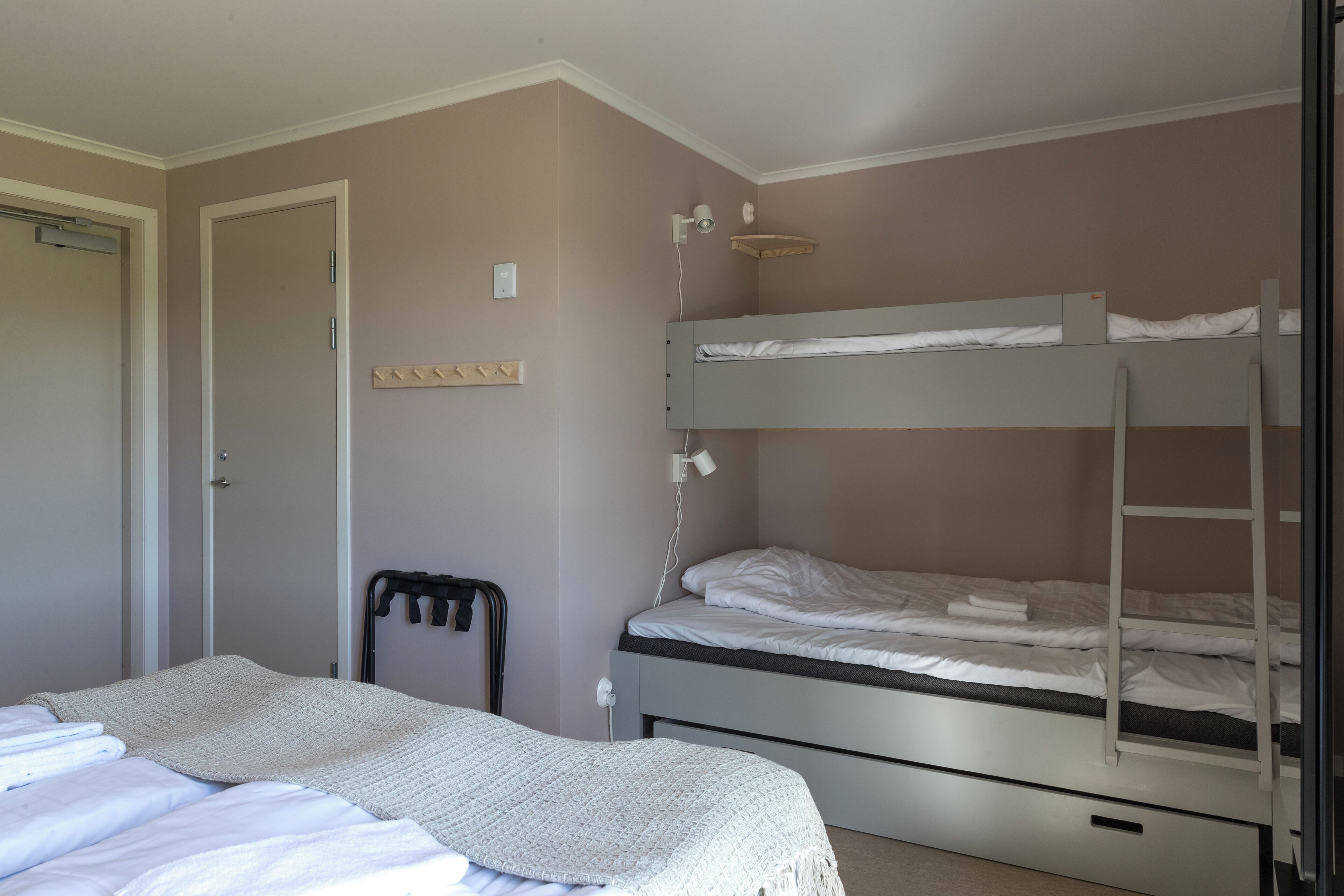 Een slaapkamer met een enkel bed, een stapelbed, een nachtkastje, een lamp en een deur.