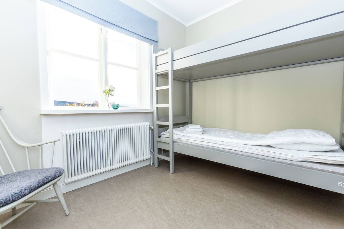 Ein Schlafraum mit Etagenbetten, einem Fenster, einer Heizung und einem Stuhl.