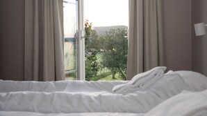 Un dormitorio con cama, ventana con cortinas y vista a un paisaje verde.