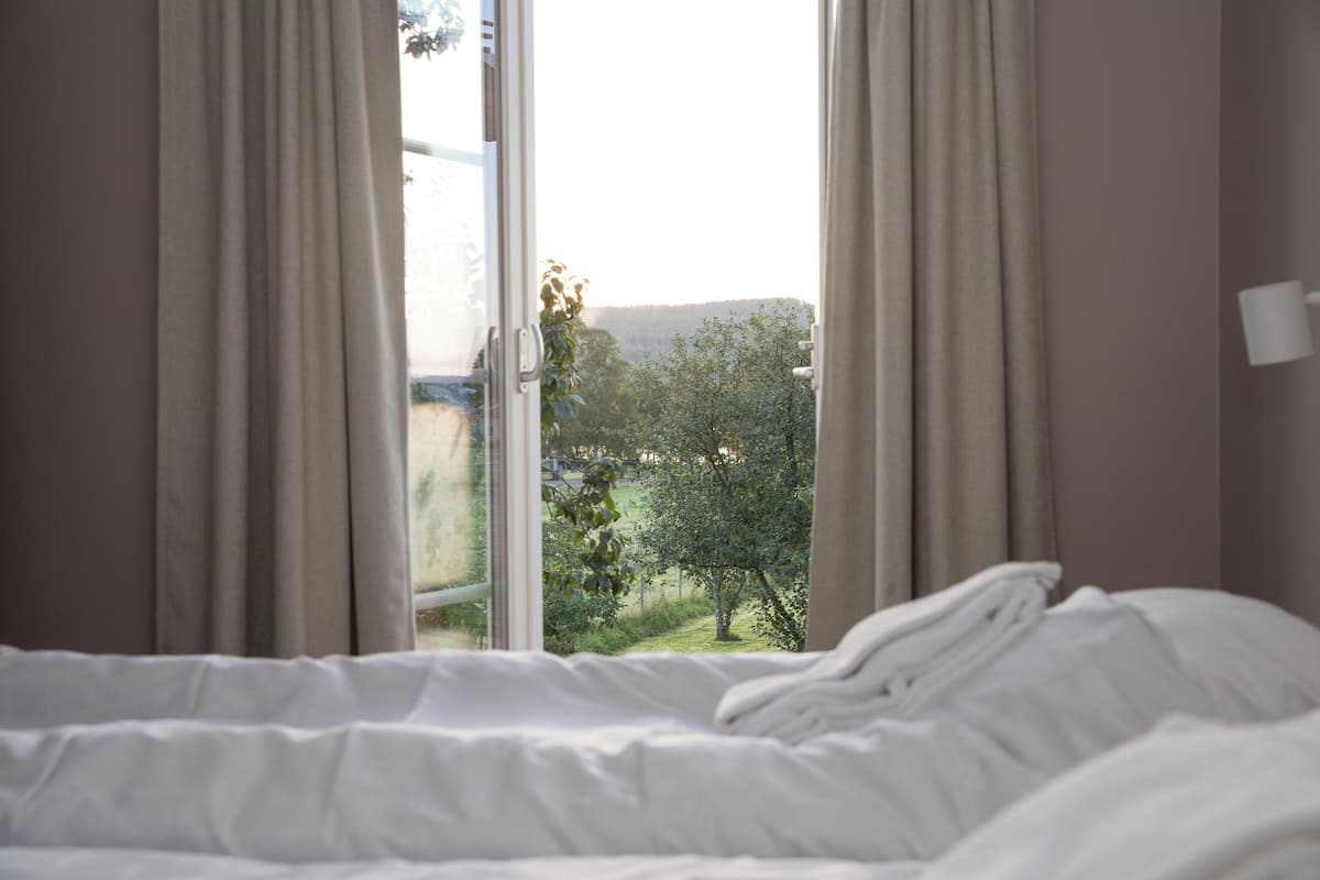 Ein Schlafzimmer mit Bett, einem Fenster mit Vorhängen und Blick auf eine grüne Landschaft.