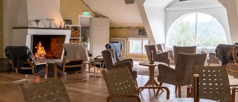 A cozy room with a fireplace, wooden furniture, and a large arched window.