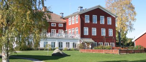 A red two-story building with a balcony, surrounded by a well-maintained lawn and trees.
