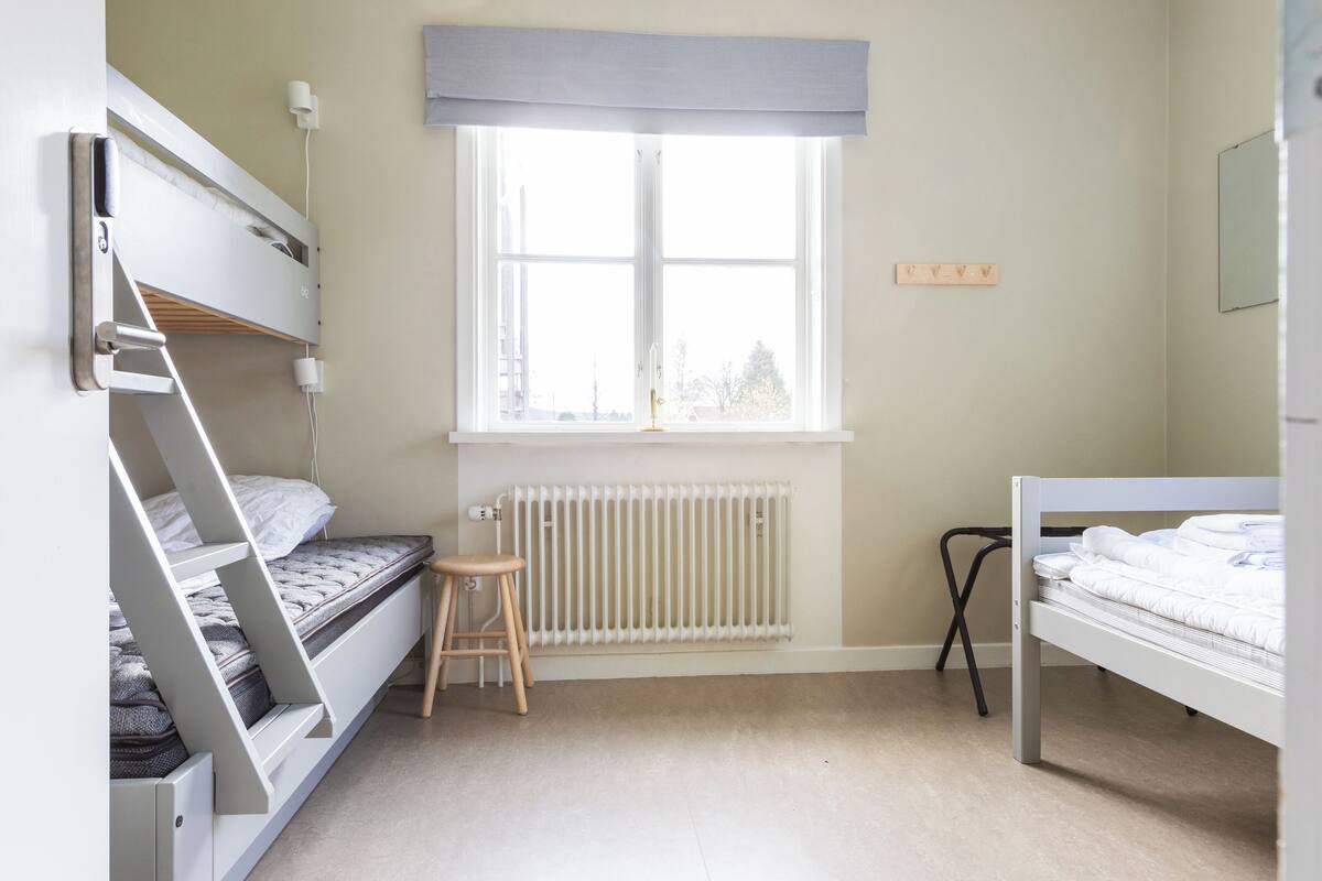 Ein Schlafzimmer mit Etagenbetten, einem Heizkörper, einem Fenster mit Blick und einem Hocker.