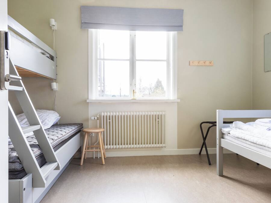 A bedroom with bunk beds, a radiator, a window with a view, and a stool.