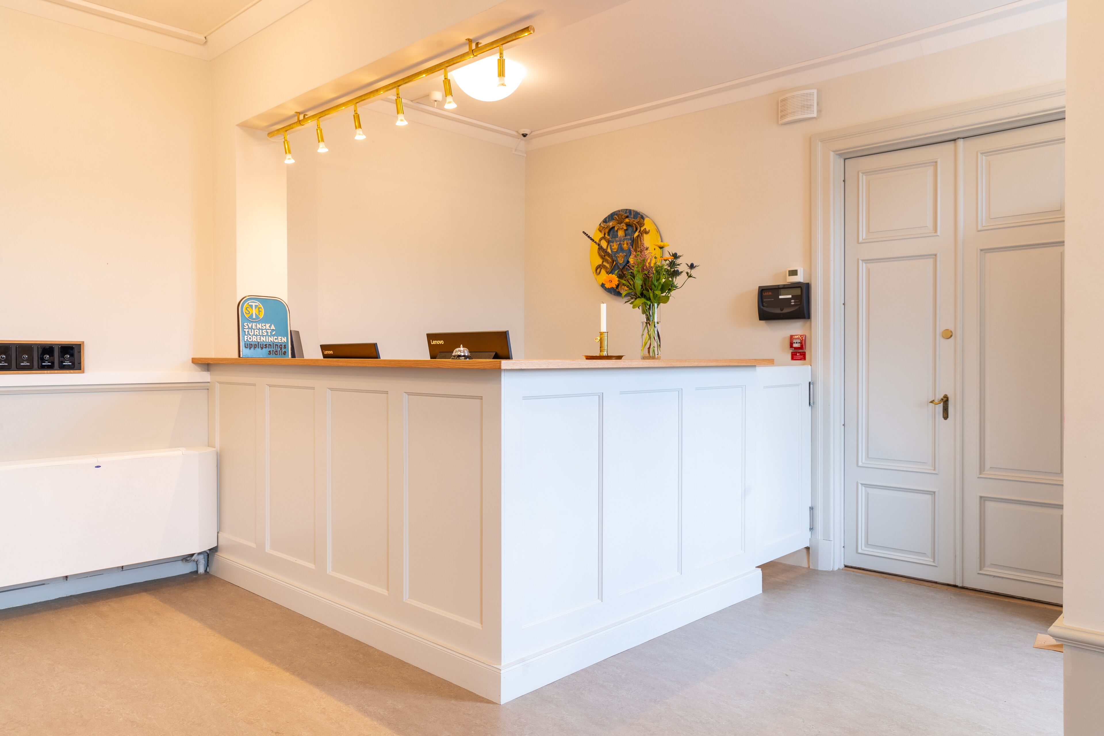 A reception area with a white reception desk, a signboard, a vase with flowers, and a door to the right.