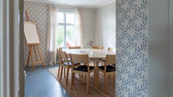 A dining room with a round table, six wooden chairs, a small easel, and a window with curtains.