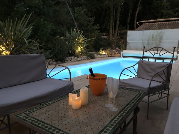 Uma área à beira da piscina com uma mesa, duas cadeiras e uma garrafa de Veuve Clicquot.