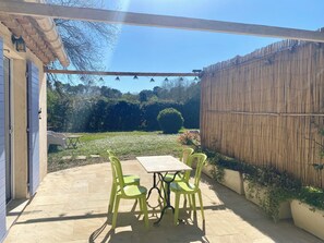 Um pátio com mesa e cadeiras, cerca de madeira e um jardim ao fundo.